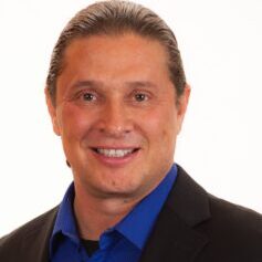 A man in a suit and blue shirt smiling for the camera.