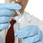 A man in blue gloves holding a test tube.